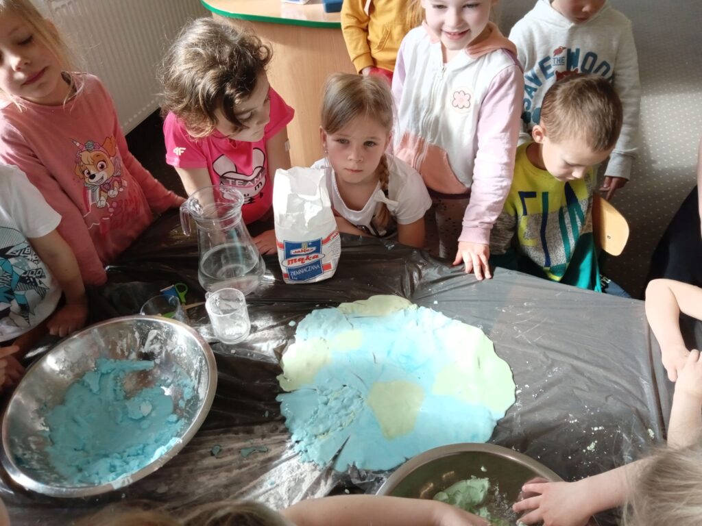 Zdjęcie przedstawia grupę dzieci przy stoliku, przygotowują się do wykonania prac plastycznych.