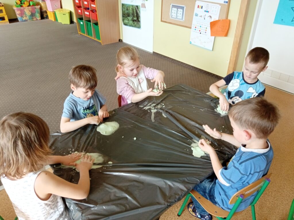 Zdjęcie przedstawia dzieci siedzące przy stolikach, wykonują prace plastyczne.