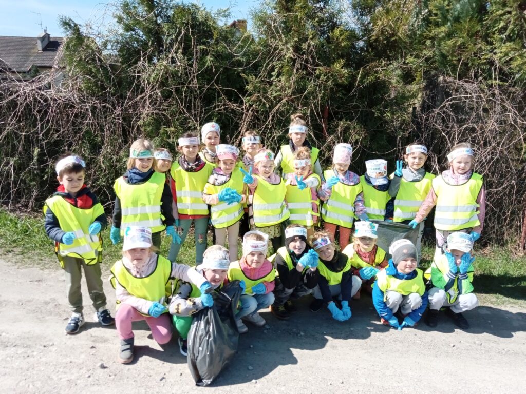 Zdjęcie przedstawia grupę dzieci w kamizelkach odblaskowych w plenerze.