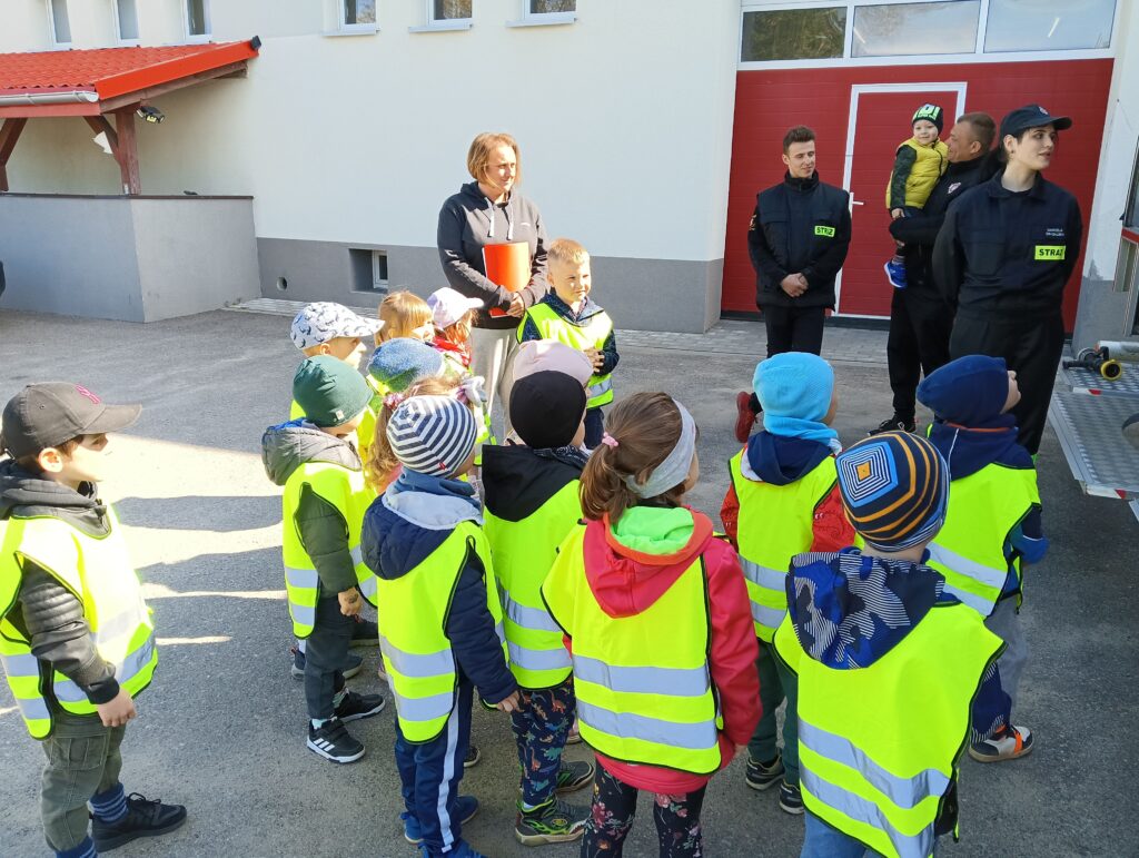 Zdjęcie przestawia grupę dzieci, opiekuna i strażaków.