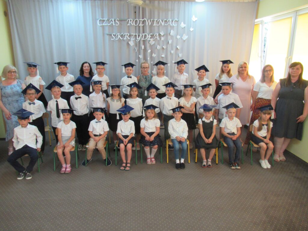 Zdjęcie przedstawia grupę dzieci i dorosłych w sali przedszkolnej.