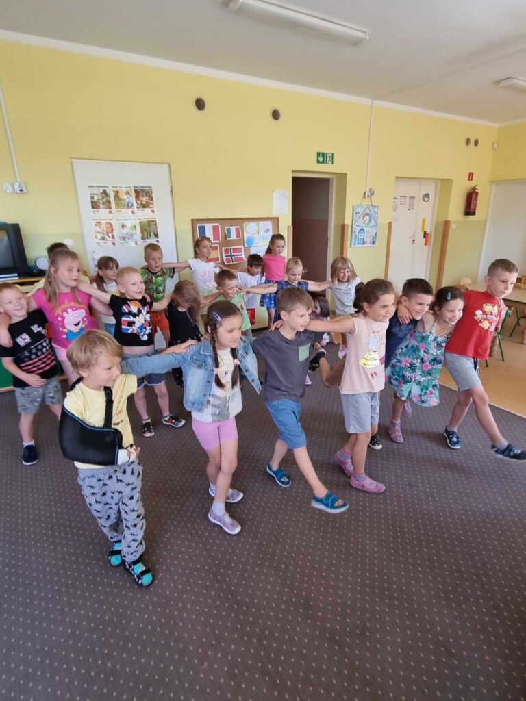 Zdjęcie przedstawia grupę tańczących dzieci w sali przedszkolnej.