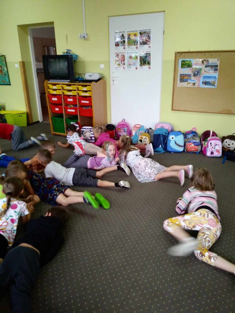 Zdjęcie przedstawia grupę dzieci bawiących się w sali przedszkolnej.