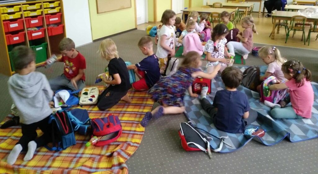 Zdjęcie przedstawia grupę dzieci bawiących się w sali przedszkolnej.