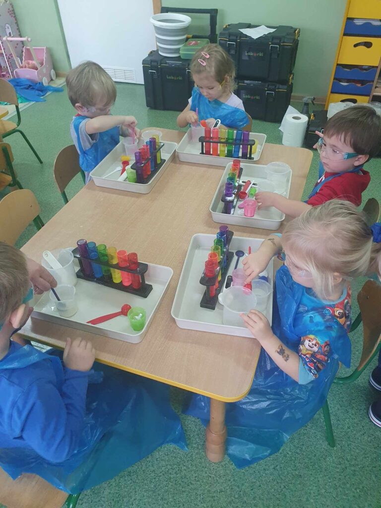 Zdjęcie przedstawia dzieci siedzące przy stoliku w sali przedszkolnej.