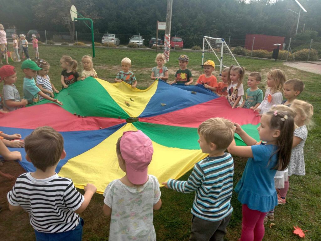 Zdjęcie przedstawia grupę dzieci bawiących się w ogrodzie przedszkolnym.