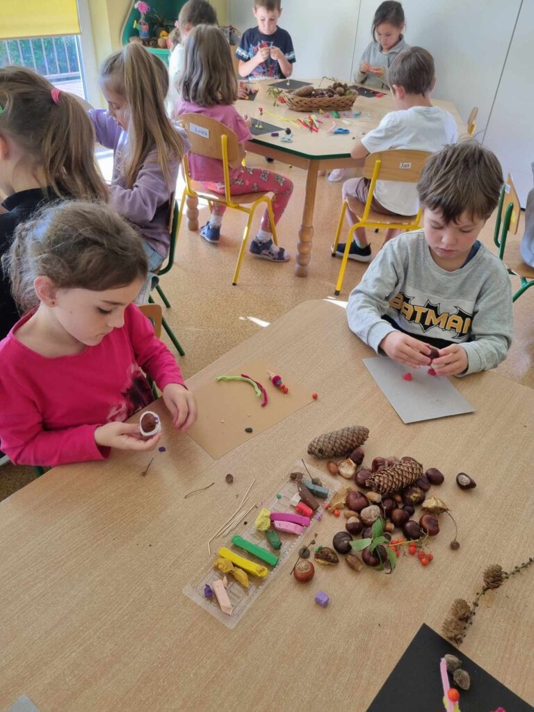 Zdjęcie przedstawia dzieci siedzące przy stolikach w sali przedszkolnej - tworzą prace plastyczne.