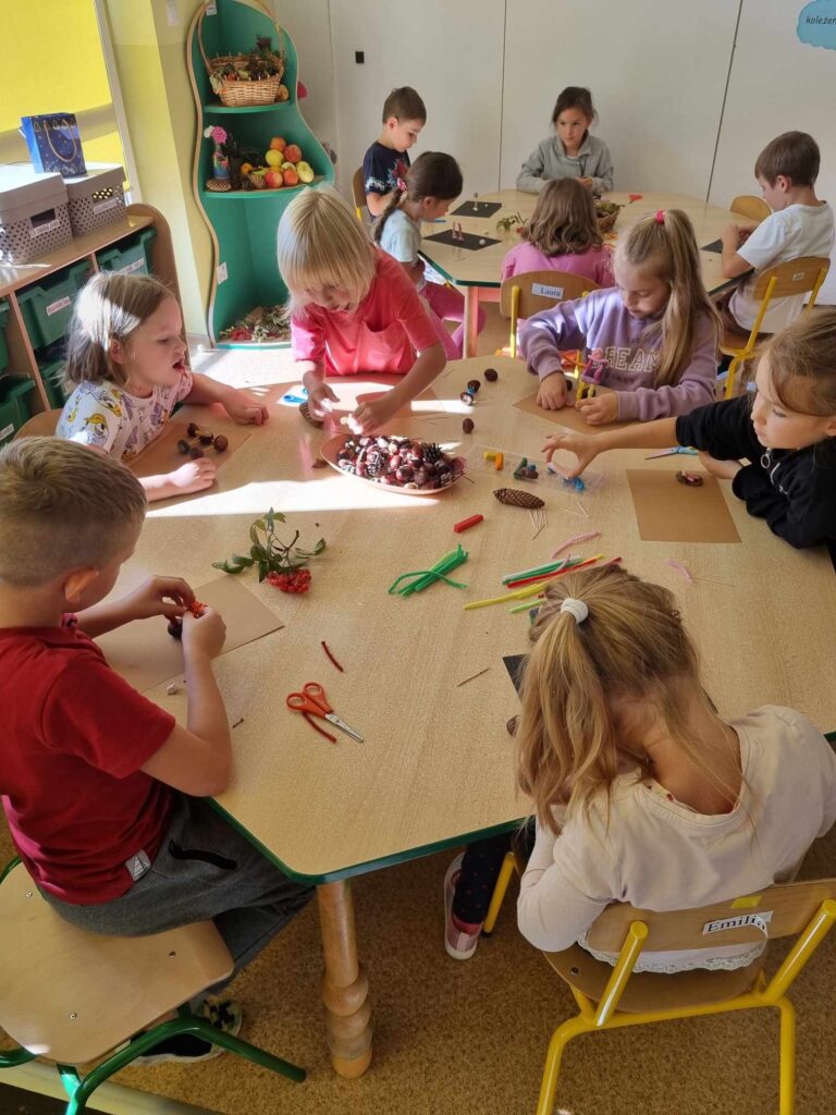 Zdjęcie przedstawia dzieci siedzące przy stolikach w sali przedszkolnej - tworzą prace plastyczne.