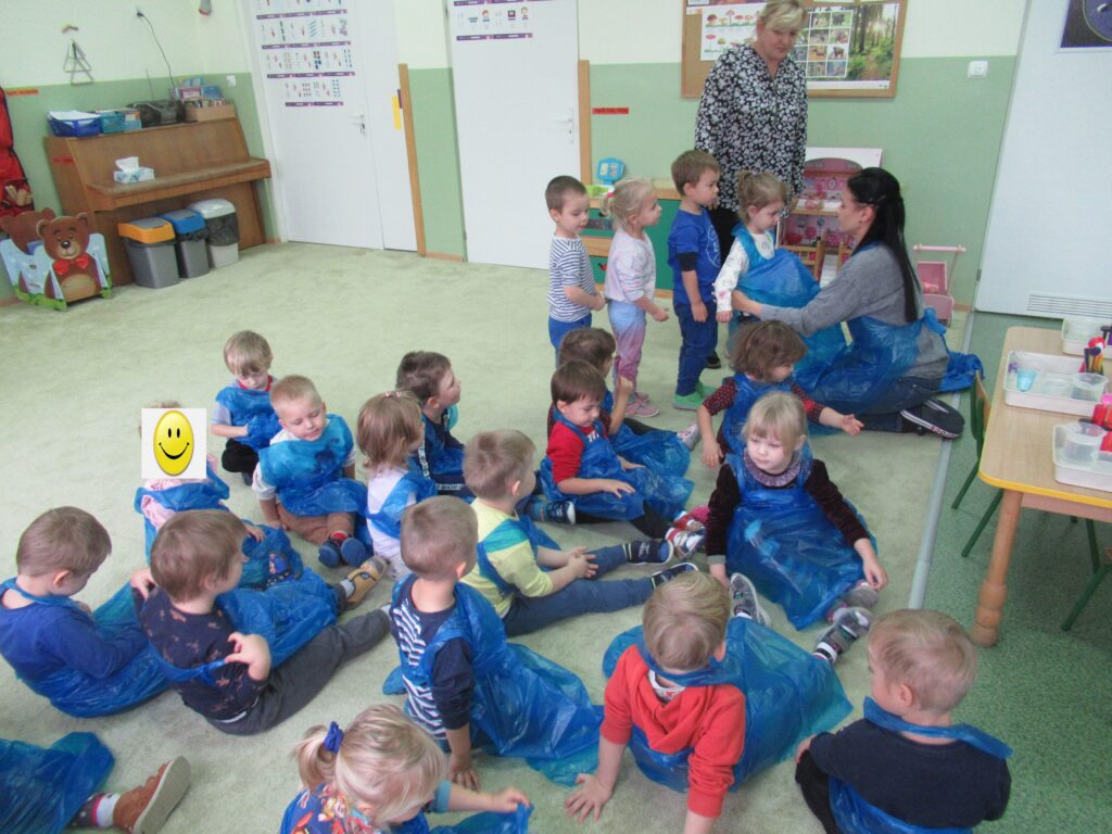 Zdjęcie przedstawia panie oraz grupę dzieci w sali przedszkolnej.