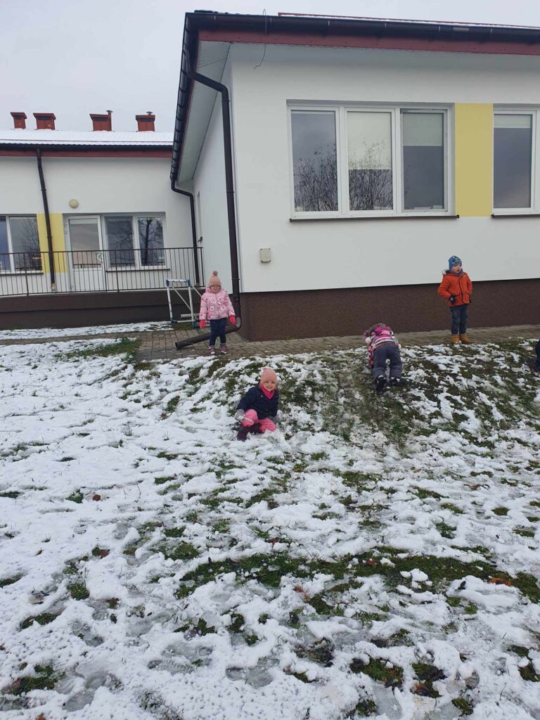 Zdjęcie przedstawia dzieci w ogrodzie przedszkolnym. W oddali widać budynek przedszkola.