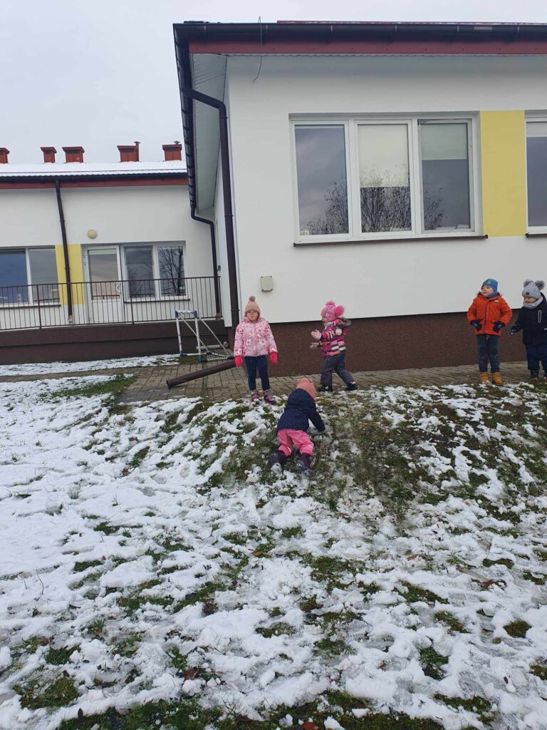 Zdjęcie przedstawia dzieci w ogrodzie przedszkolnym. W oddali widać budynek przedszkola.