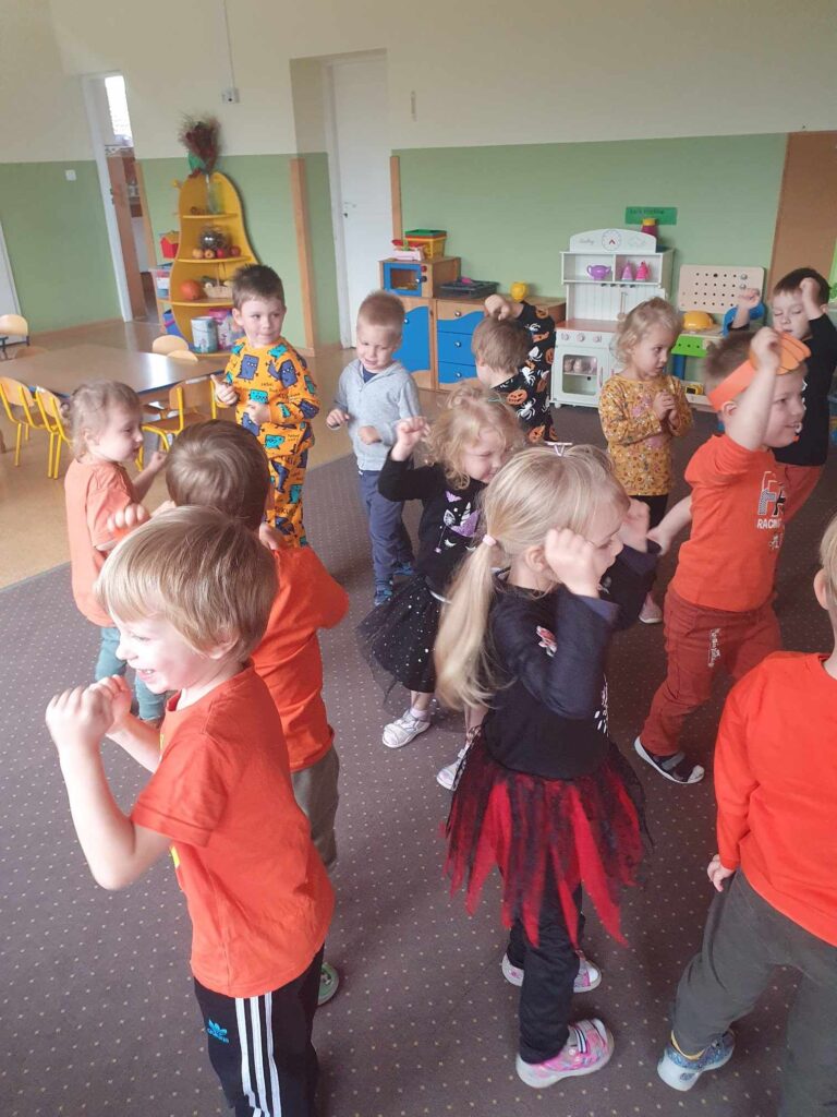 Zdjęcie przedstawia grupę bawiących się dzieci w sali przedszkolnej.