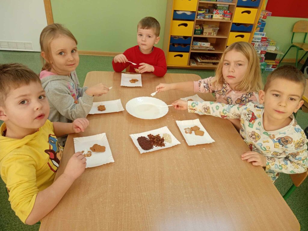 Zdjęcie przedstawia dzieci siedzące przy stoliku w sali przedszkolnej.