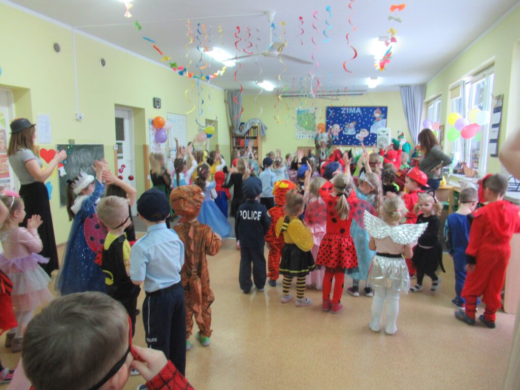 Zdjęcie przedstawia grupę bawiących się ludzi w sali przedszkolnej.