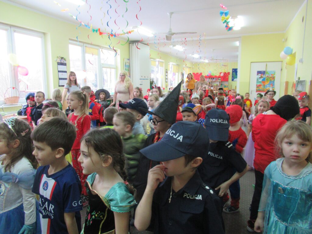 Zdjęcie przedstawia grupę bawiących się ludzi w sali przedszkolnej.