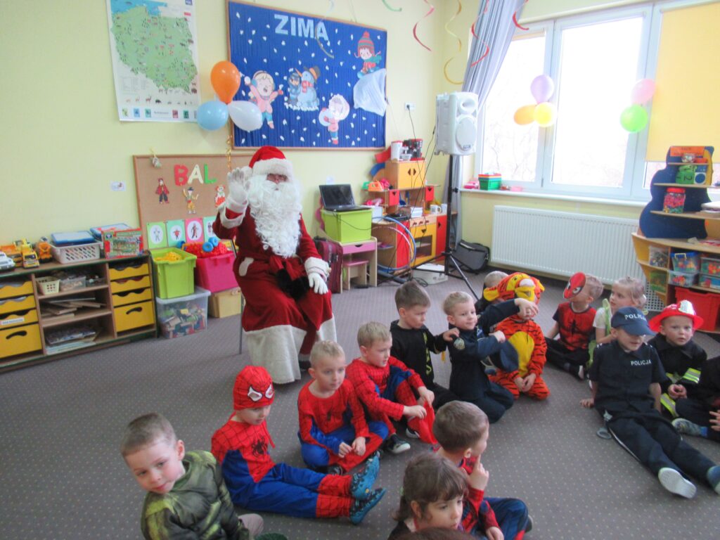 Zdjęcie przedstawia Mikołaja oraz grupę dzieci w sali przedszkolnej.