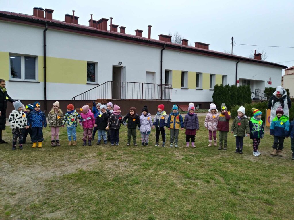 Zdjęcie przedstawia panie oraz dzieci - wszyscy witają wiosnę na placu przedszkolnym.