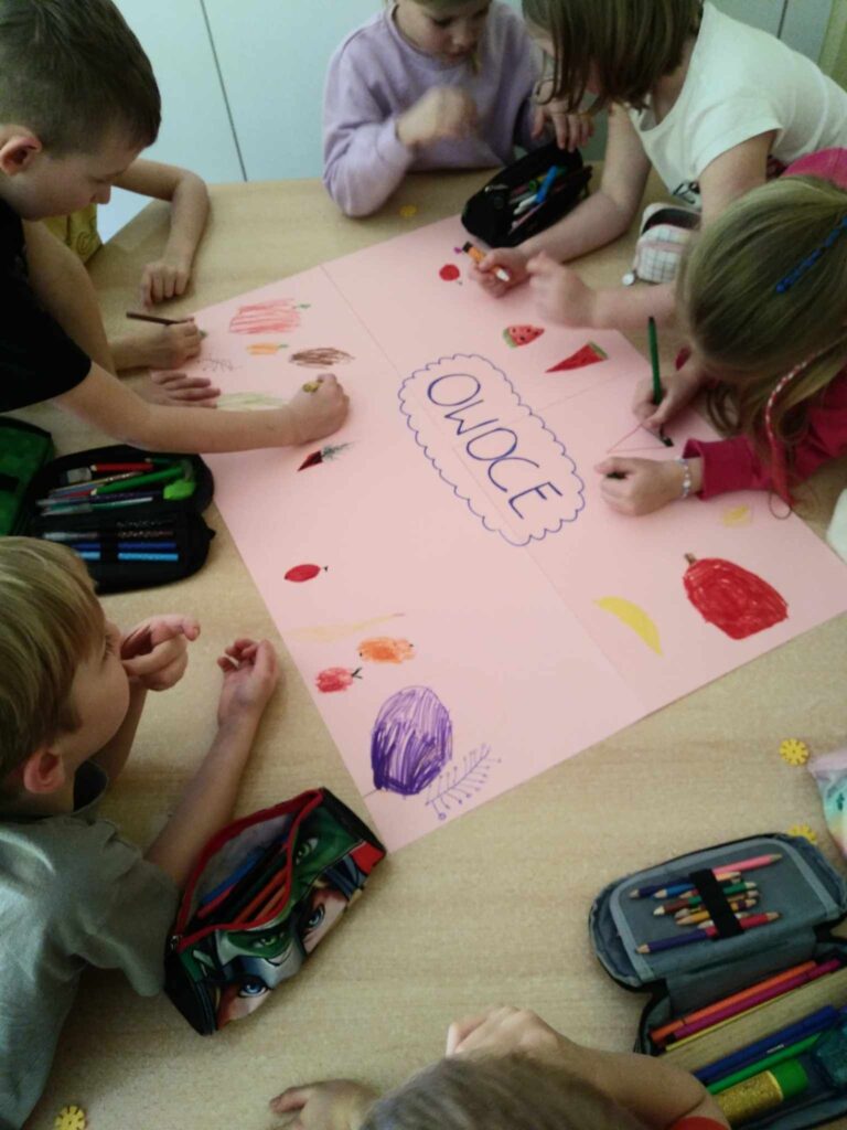 Zdjęcie przedstawia dzieci siedzące na wykładzinie w sali przedszkolnej. Dzieci wykonują duży wspólny plakat.