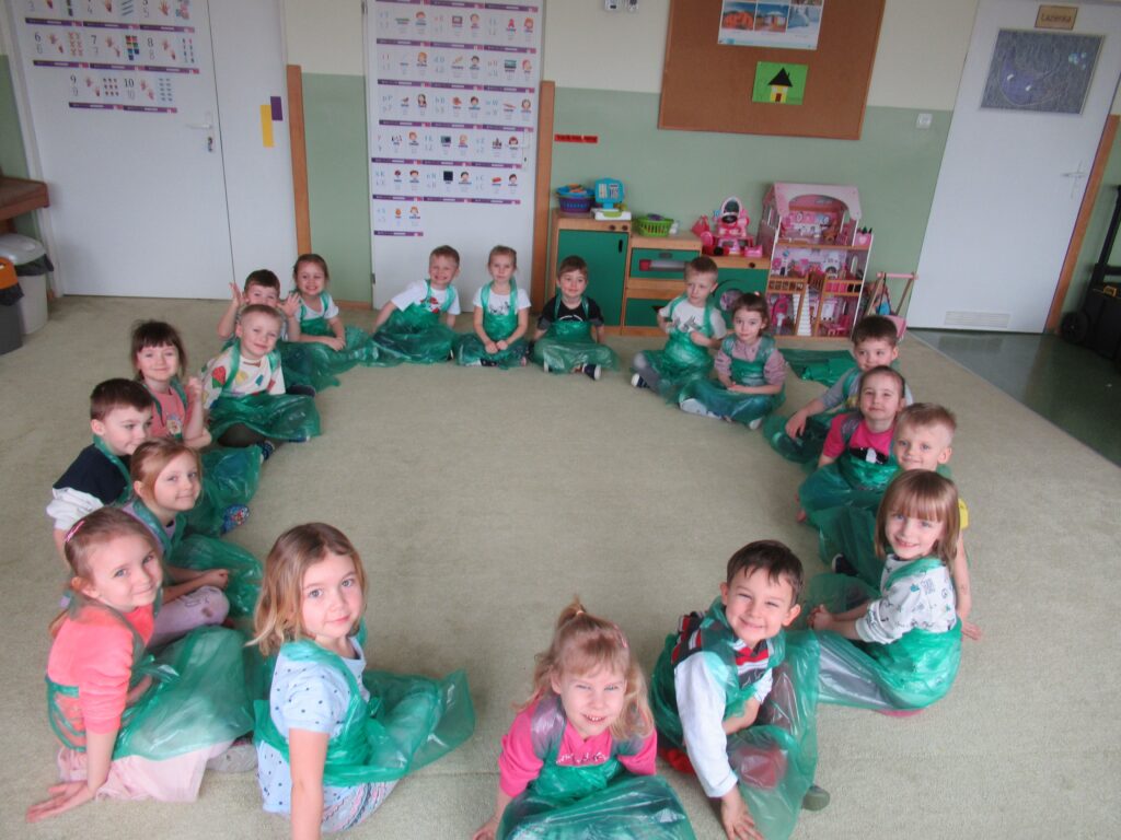 Zdjęcie przedstawia siedzące w kole dzieci w sali przedszkolnej.