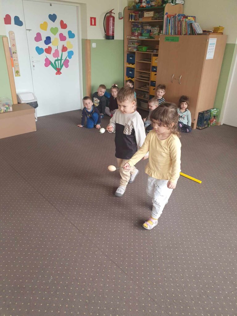 Zdjęcie przedstawia grupę bawiących się dzieci w sali przedszkolnej.