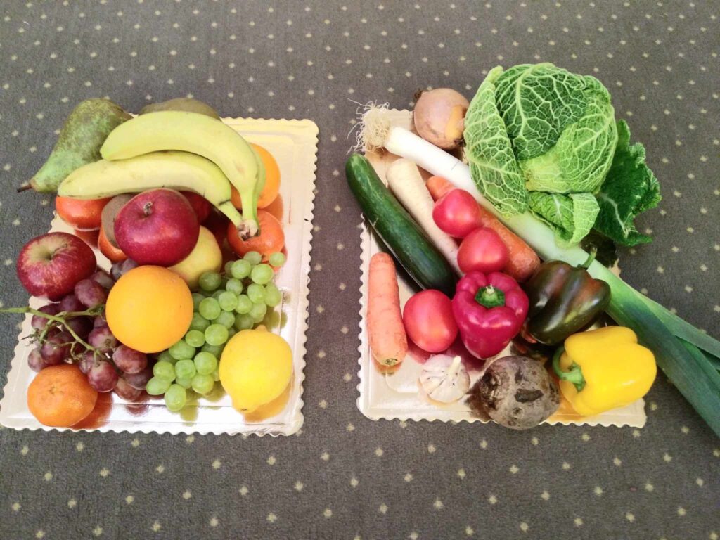 Zdjęcie przedstawia owoce i warzywa poukładane na tacach.