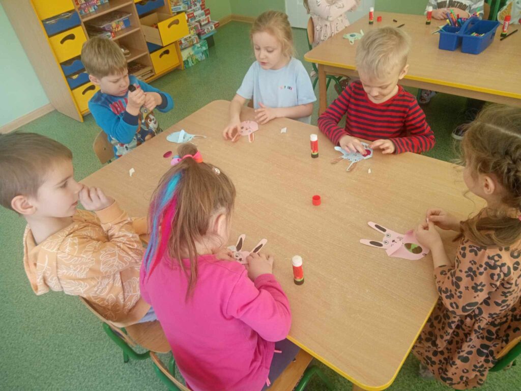 Zdjęcie przedstawia dzieci siedzące przy stoliku na zajęciach w sali przedszkolnej.