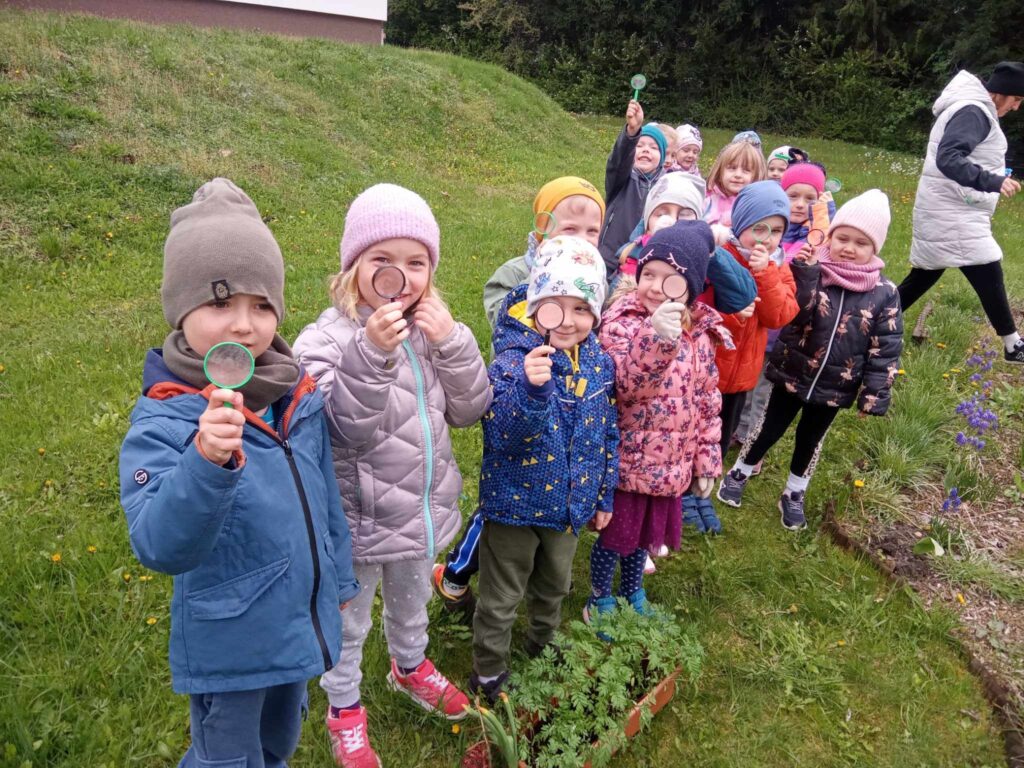 Zdjęcie przedstawia panią oraz bawiące się dzieci w ogrodzie przedszkolnym.