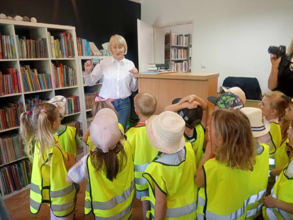 Zdjęcie przedstawia panią oraz dzieci w bibliotece.