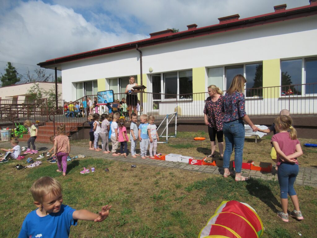 Zdjęcie przedstawia panie oraz bawiące się dzieci w ogrodzie przedszkolnym.