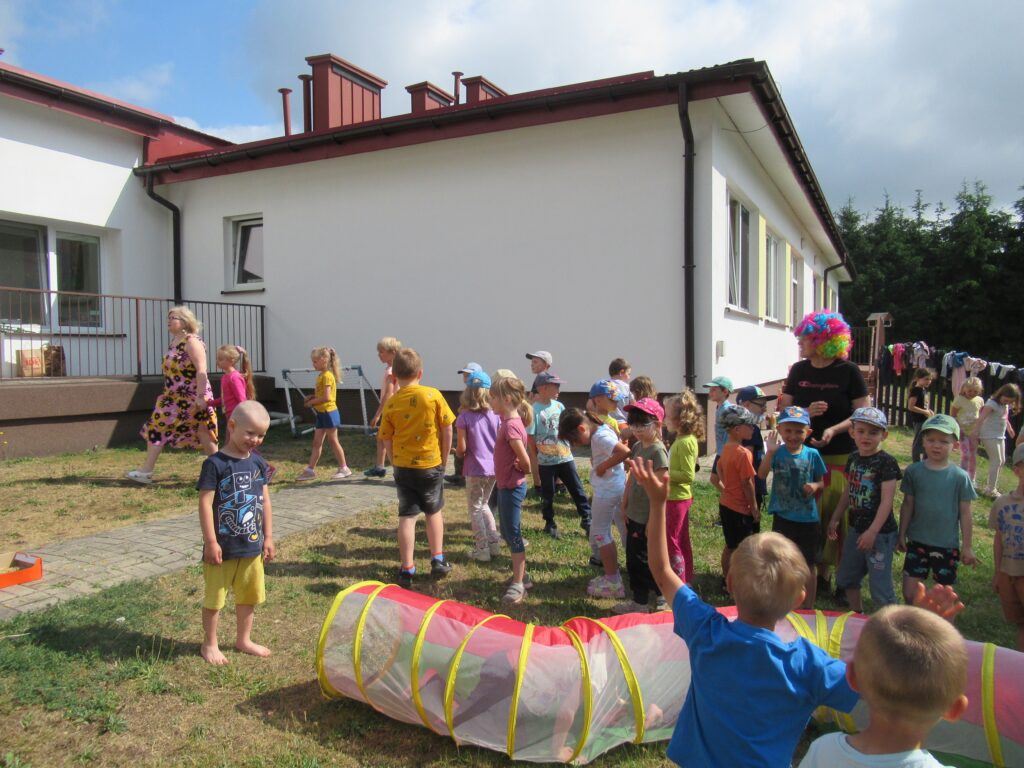 Zdjęcie przedstawia panie oraz bawiące się dzieci w ogrodzie przedszkolnym.