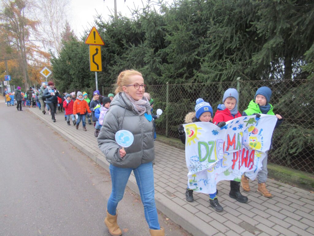 Zdjęcie przedstawia dzieci oraz panie - spacerujących ulicą.