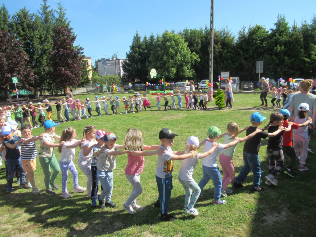 Zdjęcie przedstawia panie oraz bawiące się dzieci w ogrodzie przedszkolnym.