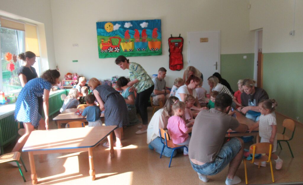 Zdjęcie przedstawia grupę ludzi w sali przedszkolnej.