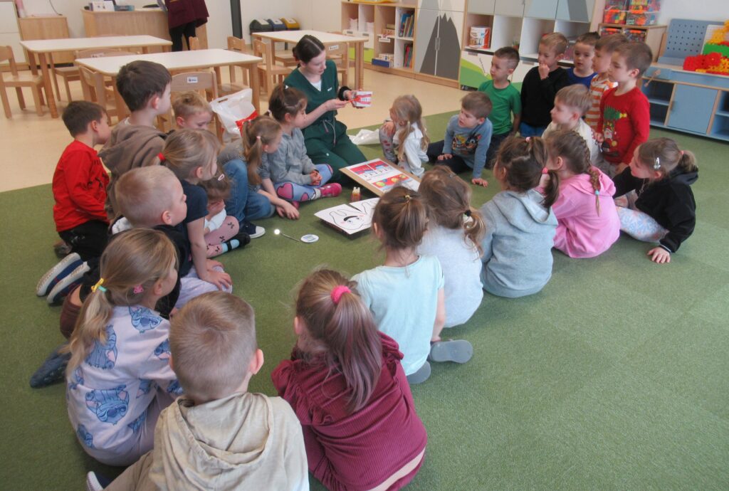 Zdjęcie przedstawia panią i dzieci w sali przedszkolnej.