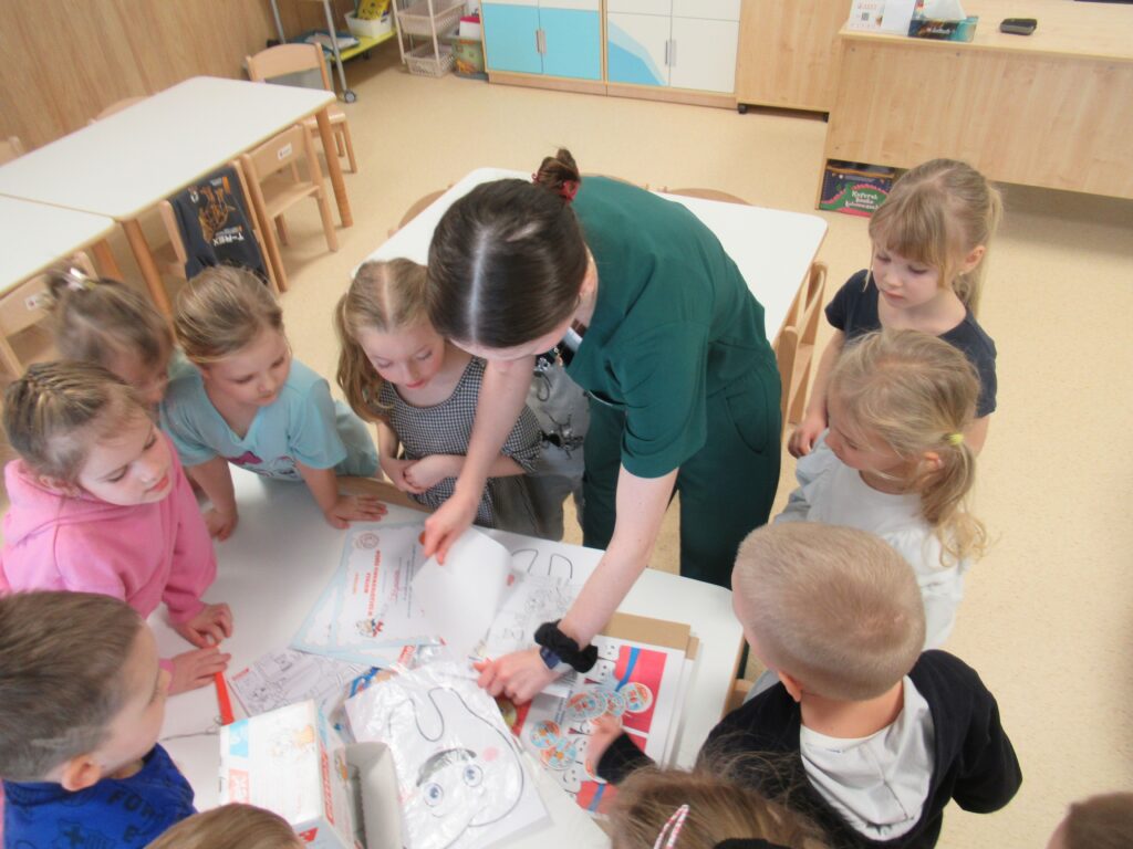 Zdjęcie przedstawia panią i dzieci w sali przedszkolnej.