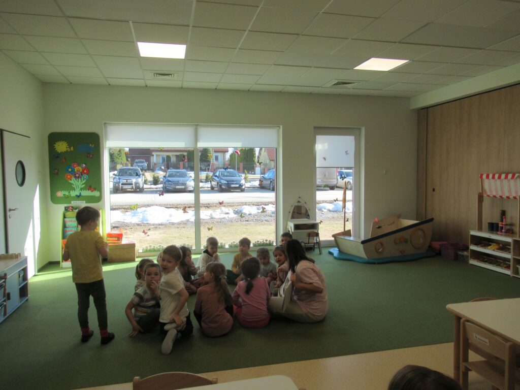 dzieci siedzą na dywanie, słuchają czytanej książki