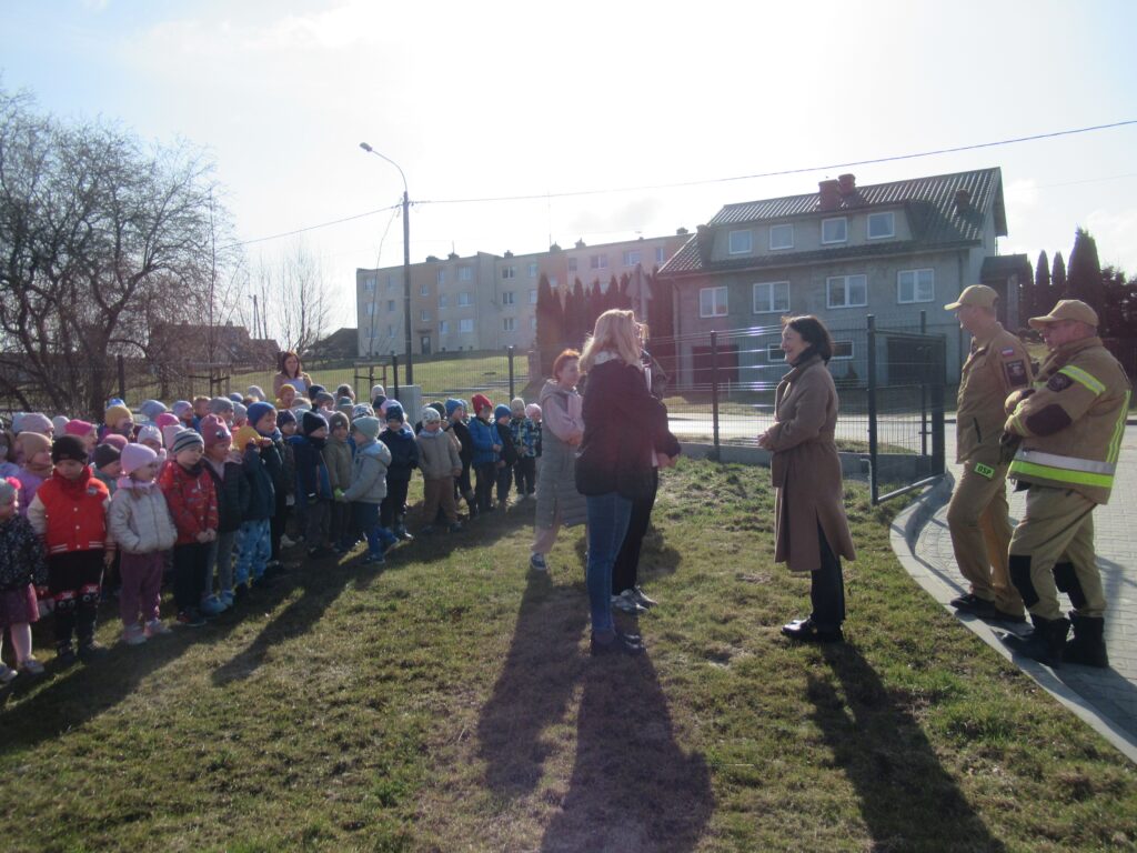 Zdjęcie przedstawia grupę ludzi. W oddali widać budynki.