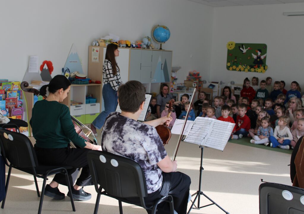 Zdjęcie przedstawia muzyków oraz słuchaczy w sali przedszkolnej.