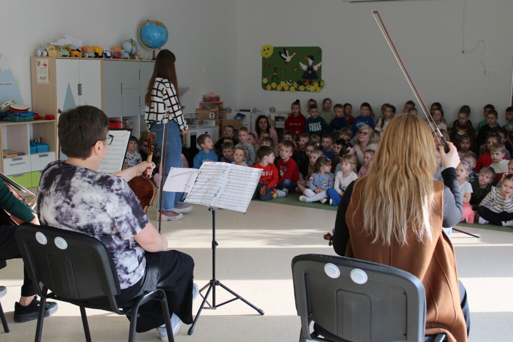 Zdjęcie przedstawia muzyków oraz słuchaczy w sali przedszkolnej.