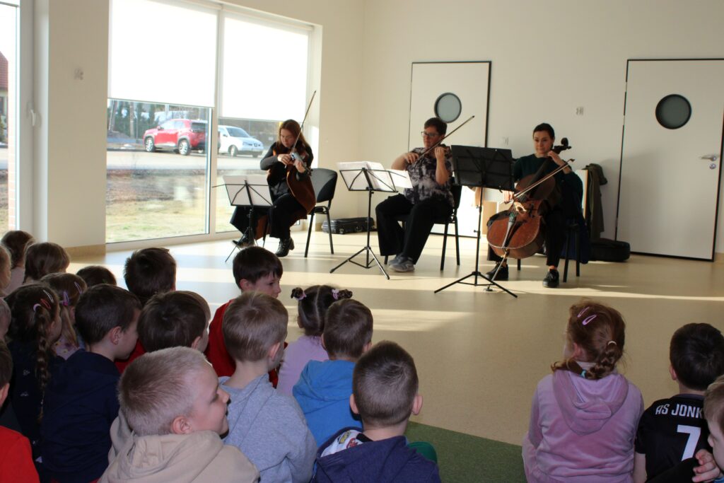 Zdjęcie przedstawia muzyków oraz dzieci w sali przedszkolnej.