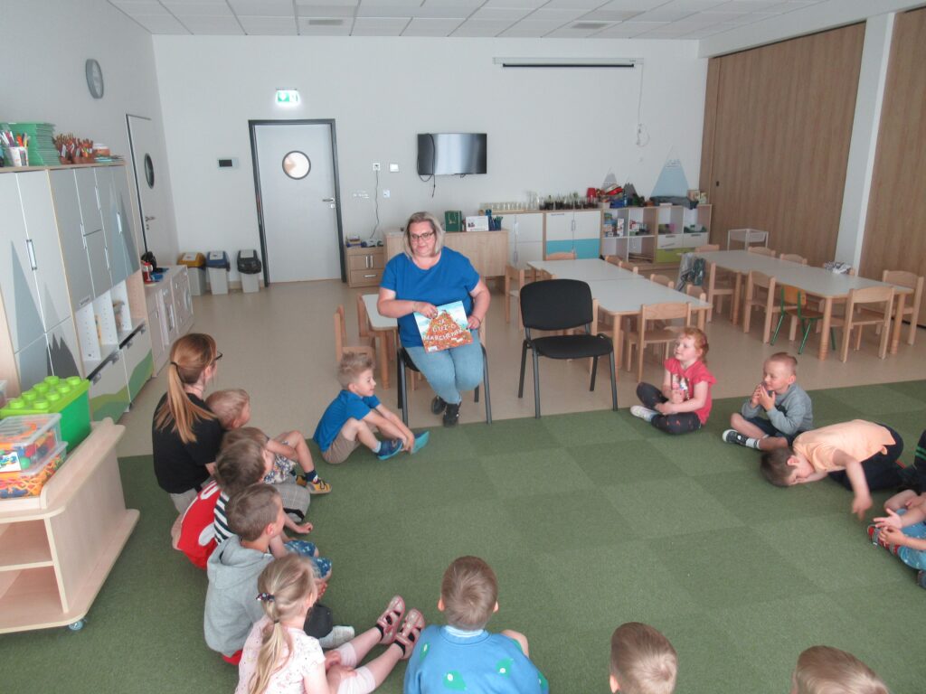 Dzieci siedzą w kole. Pani czyta książkę.