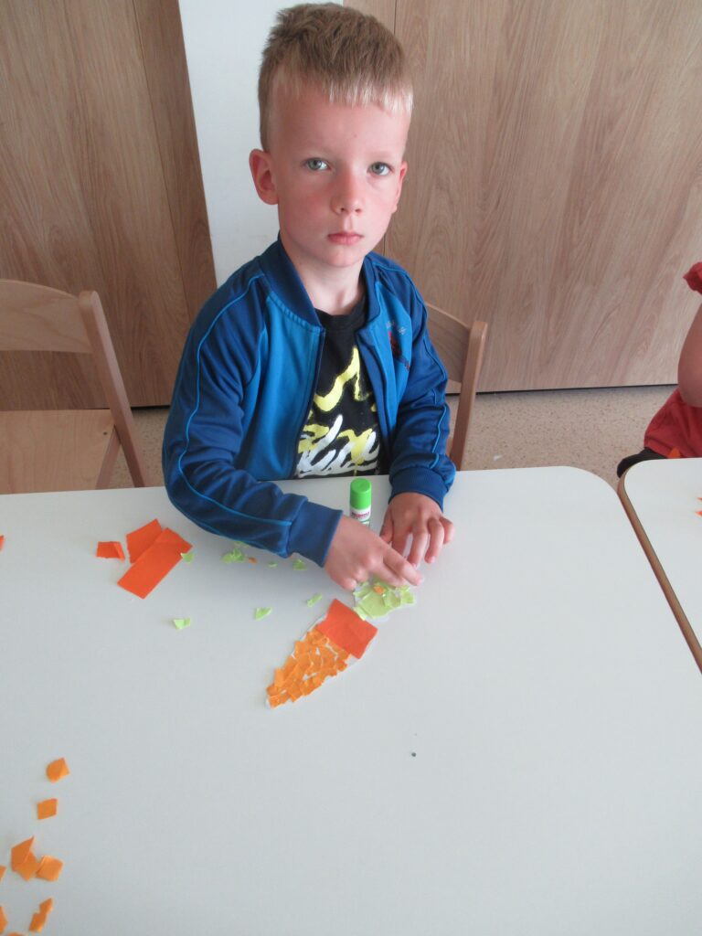 Dziecko wykonuje marchewkę z pasków papieru.