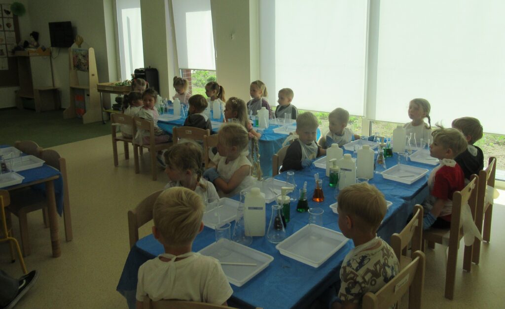 Zdjęcie przedstawia dzieci siedzących przy stolikach.