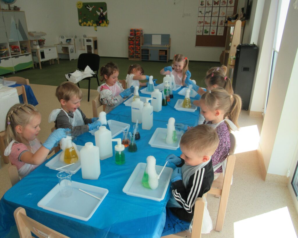 Zdjęcie przedstawia dzieci siedzących przy stolikach.