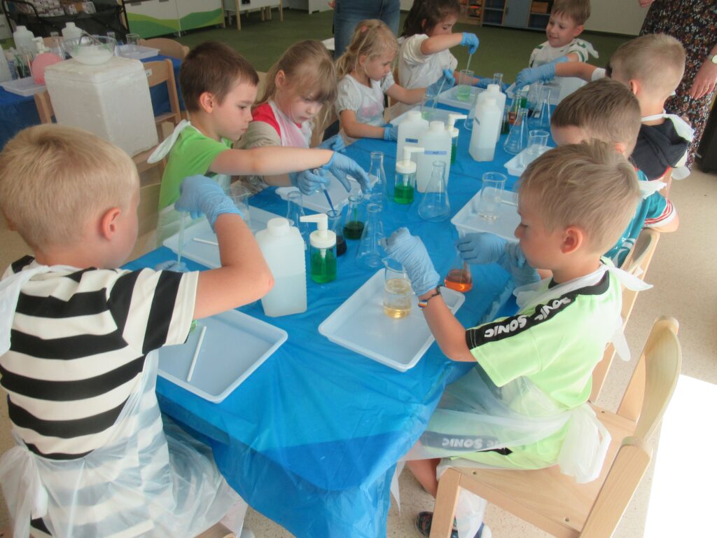 Zdjęcie przedstawia dzieci siedzących przy stolikach.