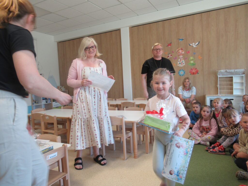 Dziecko odbiera nagrodę i dyplom od nauczycieli.