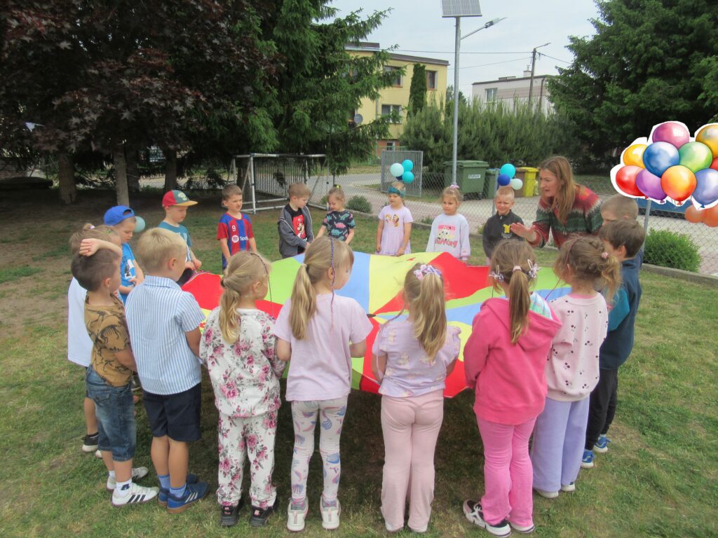Zdjęcie przedstawia panią oraz grupę dzieci w ogrodzie przedszkolnym.
